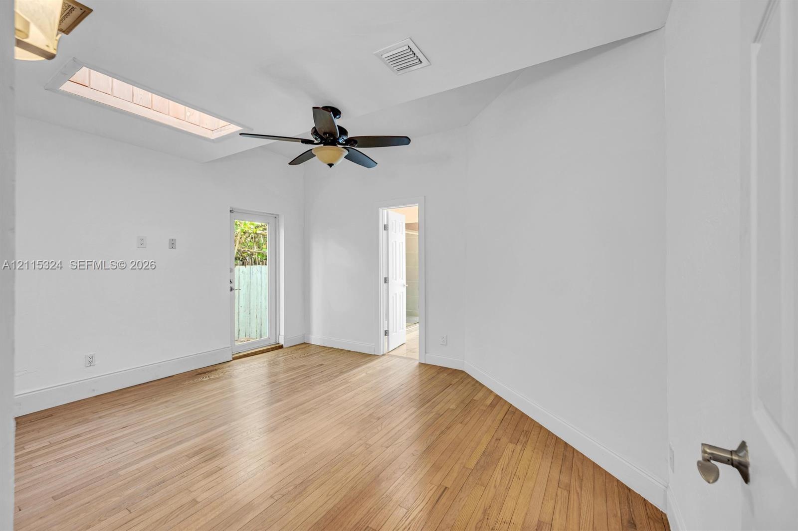 Interior space featuring wood-finish flooring, a vaulted ceiling with a skylight, a ceiling fan with integrated lighting, and an exterior glass-panel 