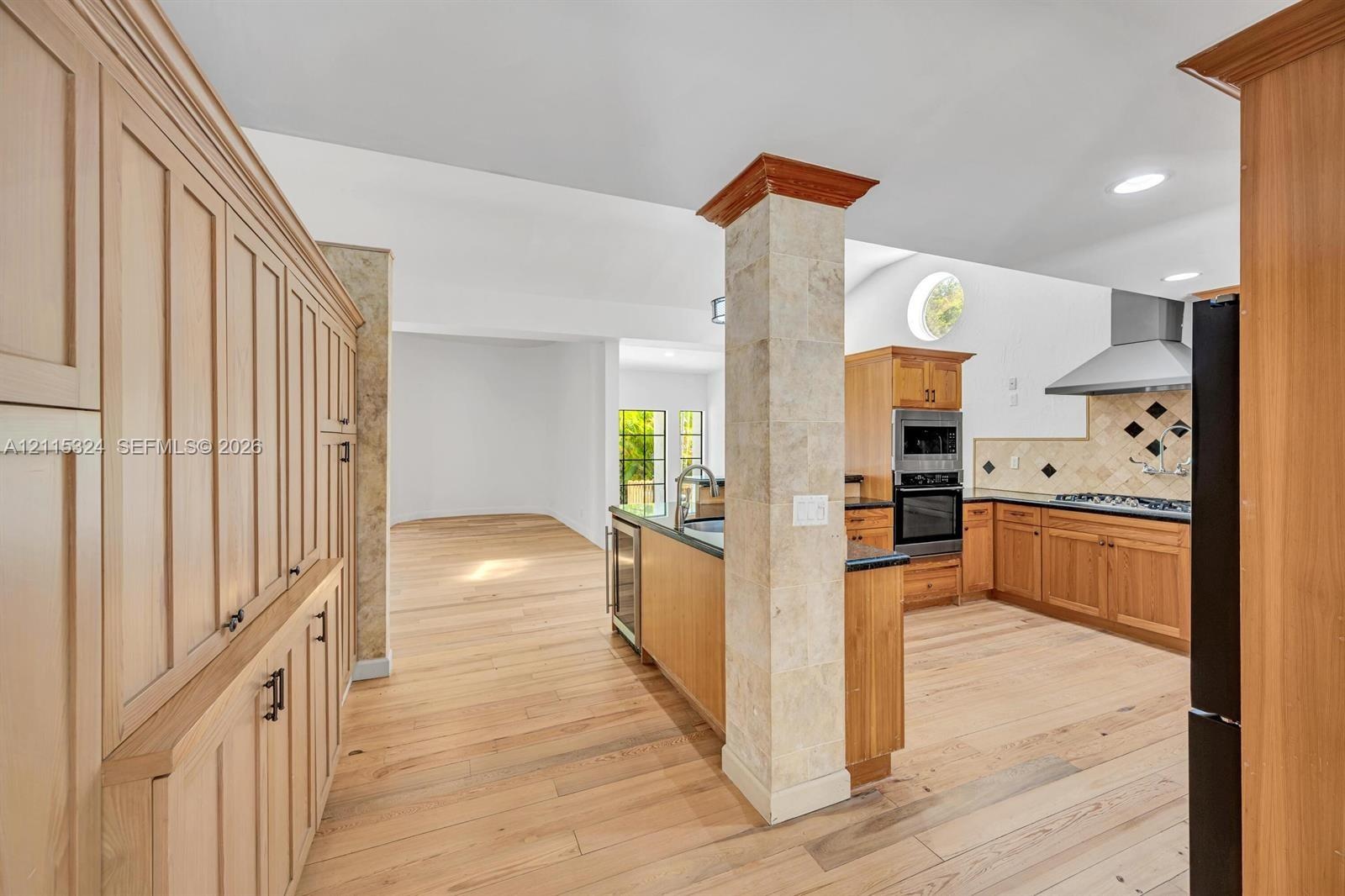 Kitchen featuring custom wood cabinetry, stone-clad structural pillar, wood-finish flooring, built-in double oven, and stainless steel vent hood