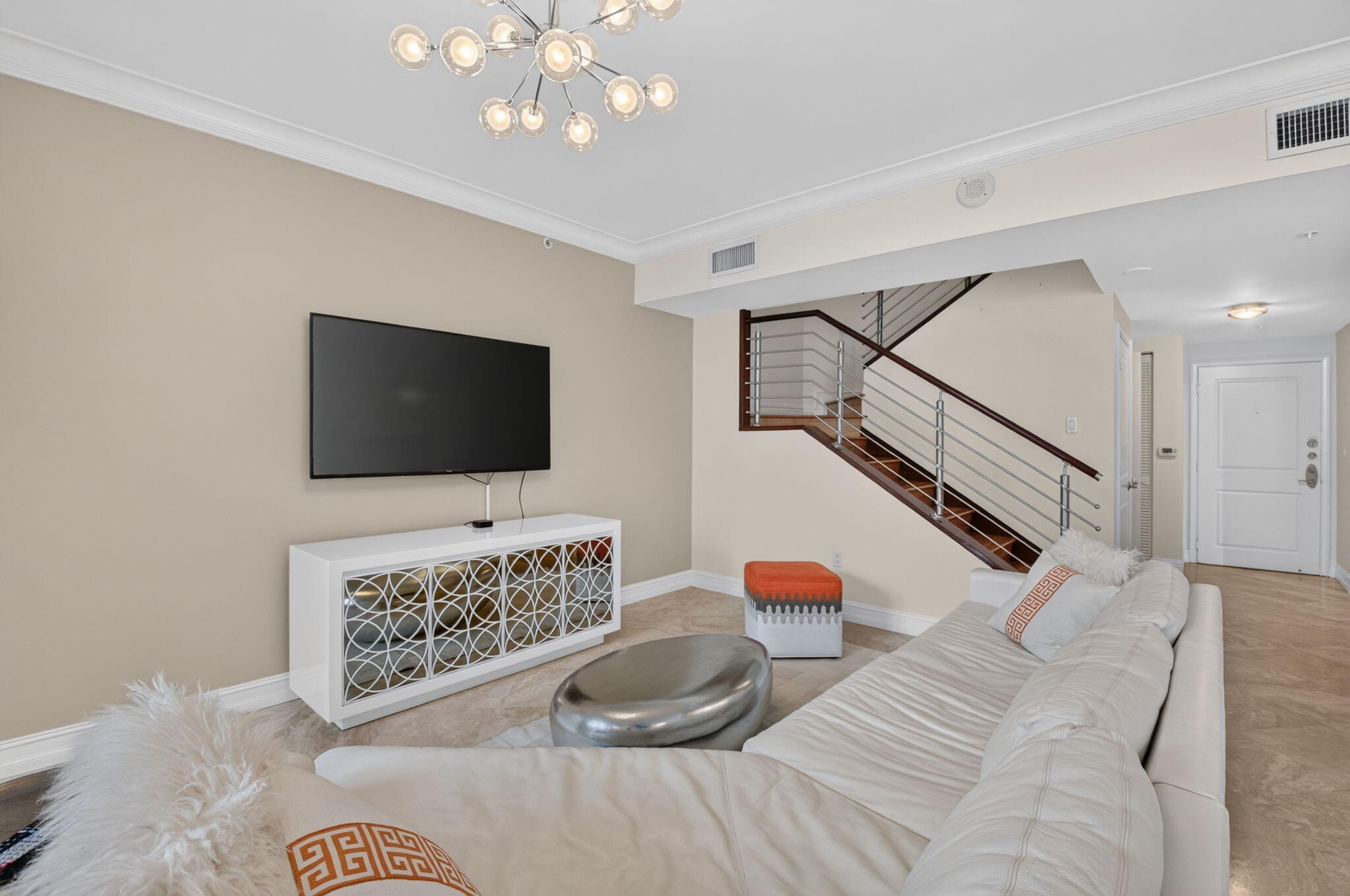 Contemporary lighting, crown molding, and wood-finish staircase with metal railings.
