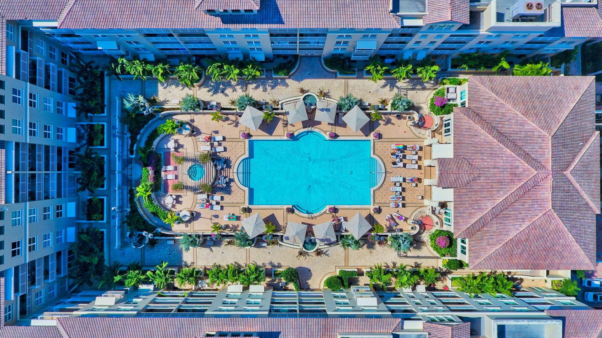 Resort-style courtyard featuring a large swimming pool, surrounding lounge areas, and lush landscaping