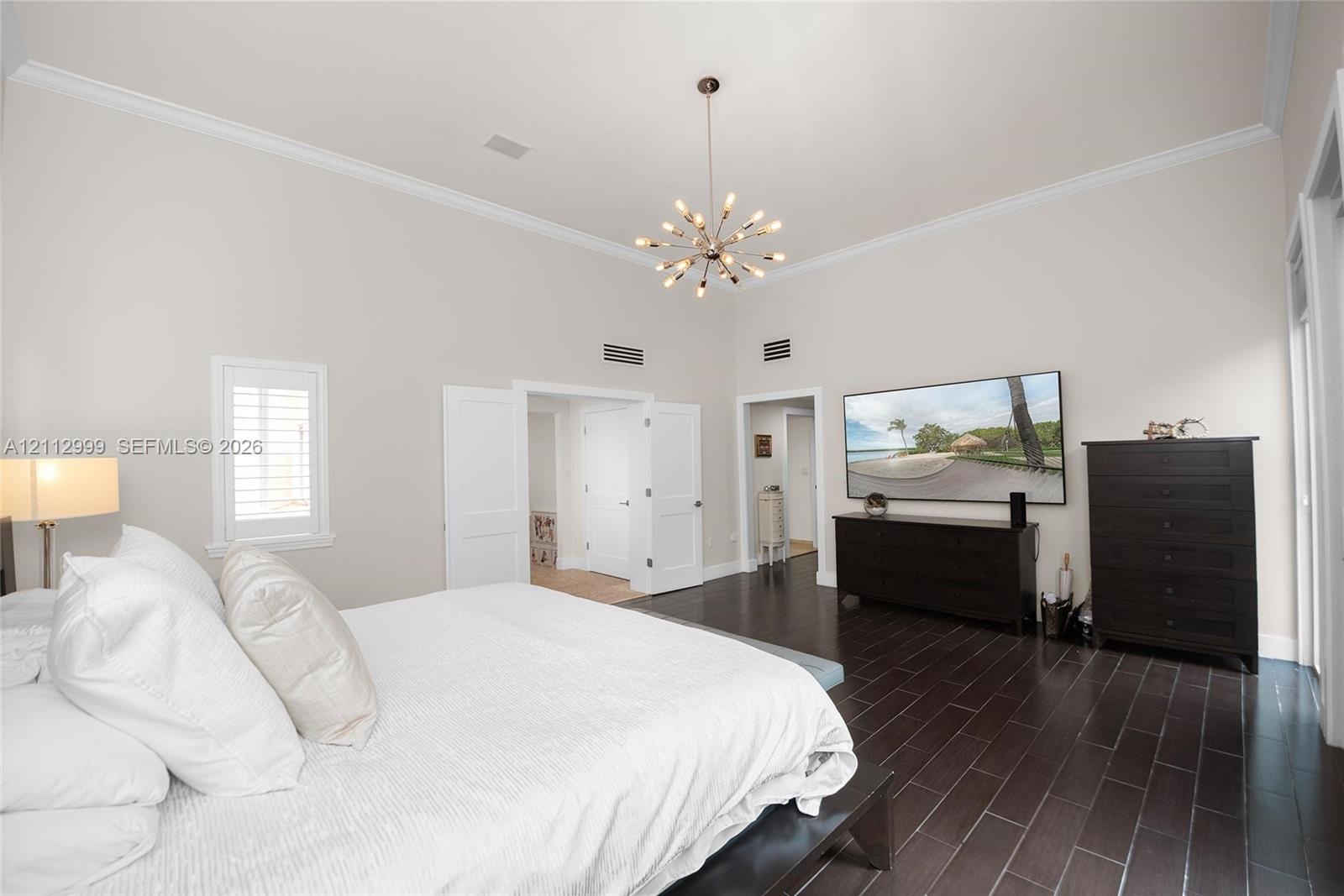 High ceilings featuring crown molding, dark wood-finish flooring, and a modern sputnik-style chandelier