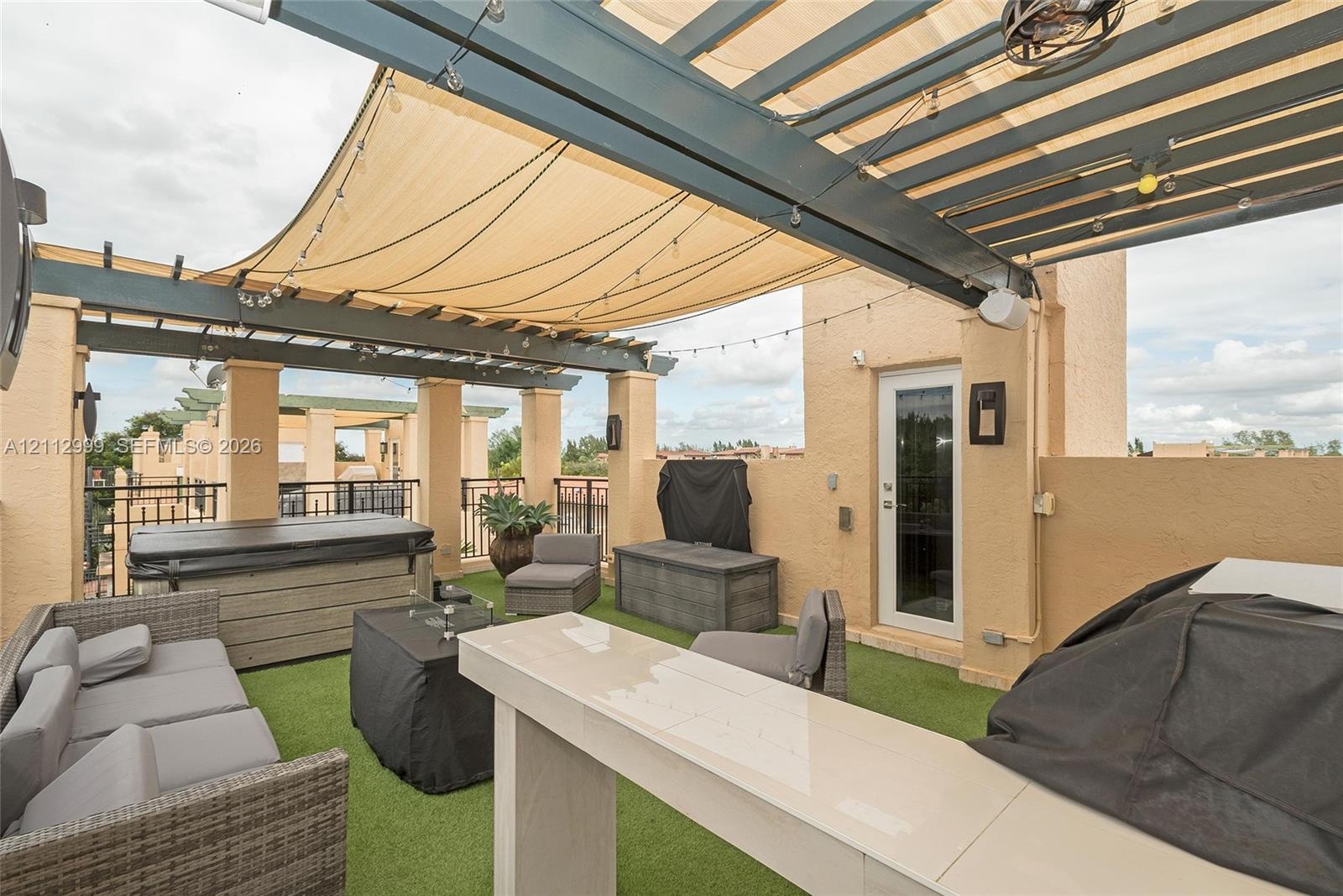 Rooftop terrace featuring a custom metal pergola with integrated shade canopy, built-in bar, artificial turf flooring, and a recessed spa