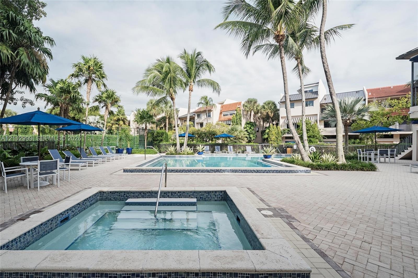 Outdoor swimming pool and spa featuring a stone-paver deck, built-in steps, and surrounding palm trees