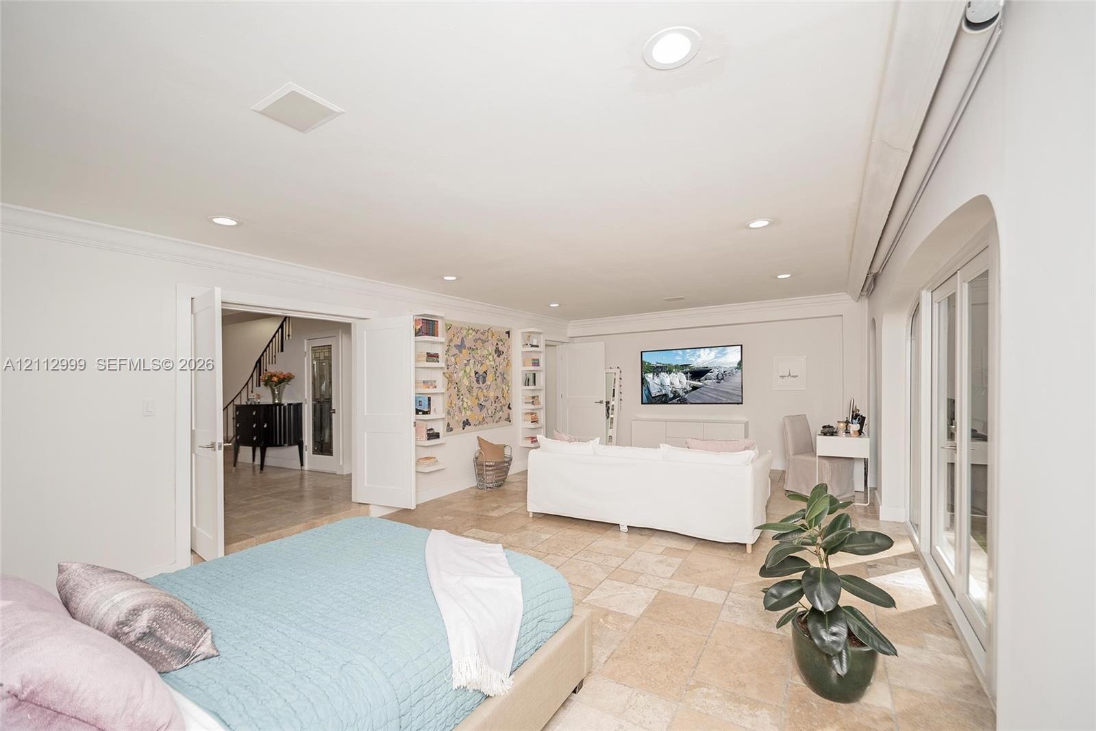 Neutral-toned stone flooring, recessed lighting, double French doors, and built-in shelving units