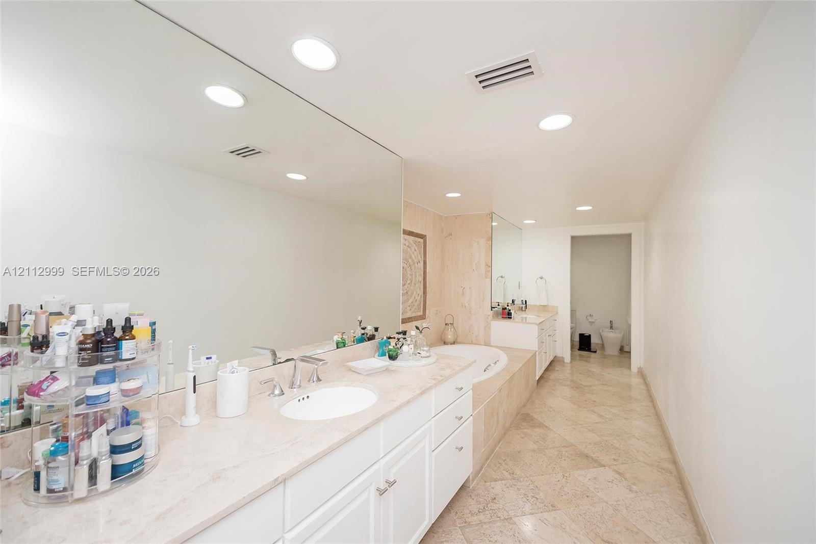 Dual vanity with stone countertop, large wall-mounted mirror, recessed lighting, and tile flooring
