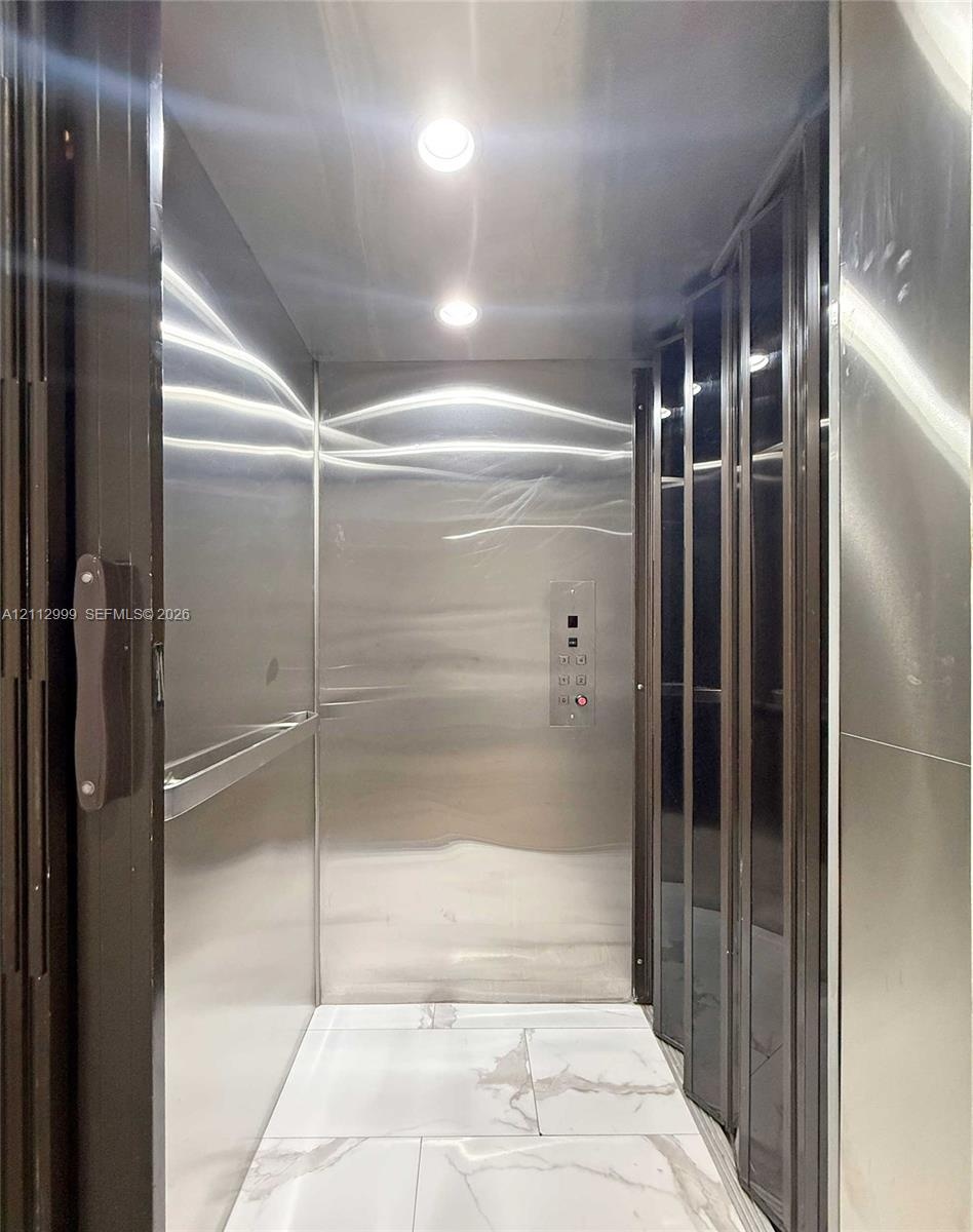 Private elevator featuring polished stainless steel wall panels, recessed ceiling lighting, a horizontal handrail, and large-format tile flooring with