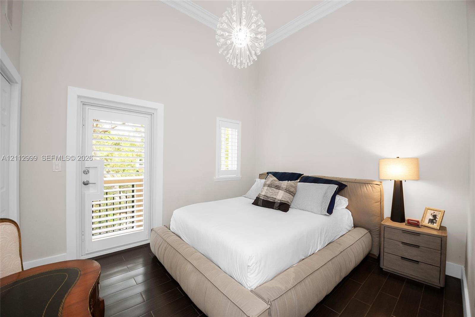 High-ceiling room featuring dark wood-finish flooring, crown molding, a multi-faceted crystal-style pendant light, and a door with integrated shuttere