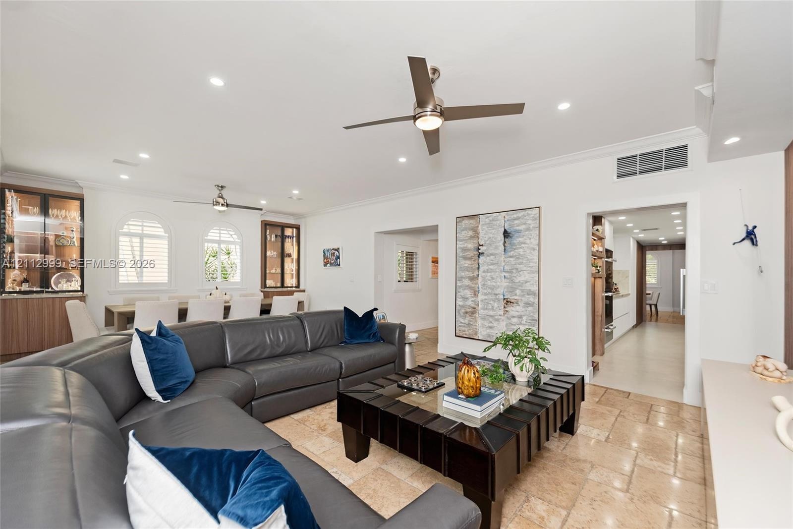 Open-concept interior featuring natural stone flooring, recessed lighting, ceiling fans, arched windows, and built-in cabinetry with glass-front displ