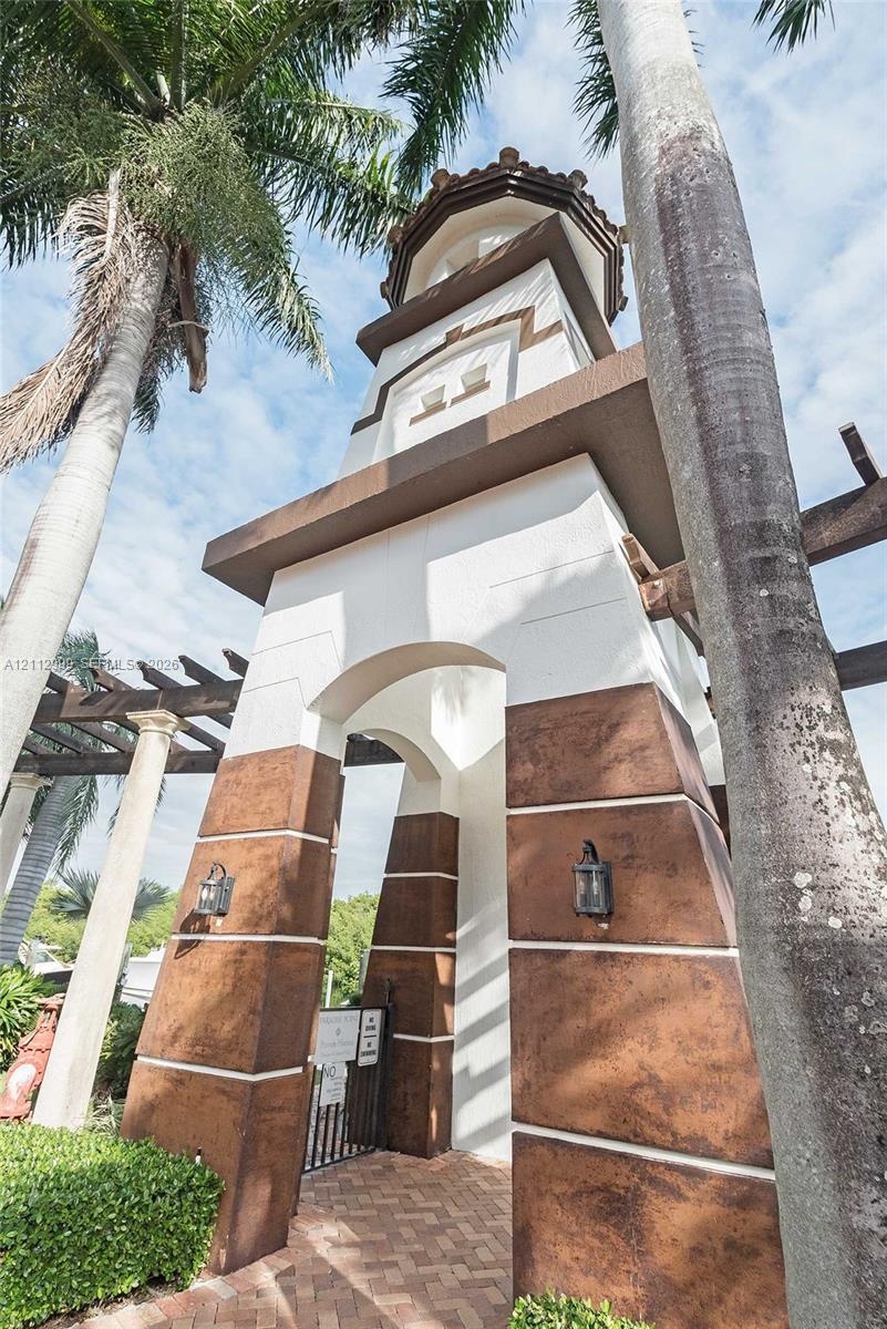 Architectural tower featuring a stucco exterior, decorative stone-finish base, arched entryway, and attached lantern-style lighting fixtures, set atop