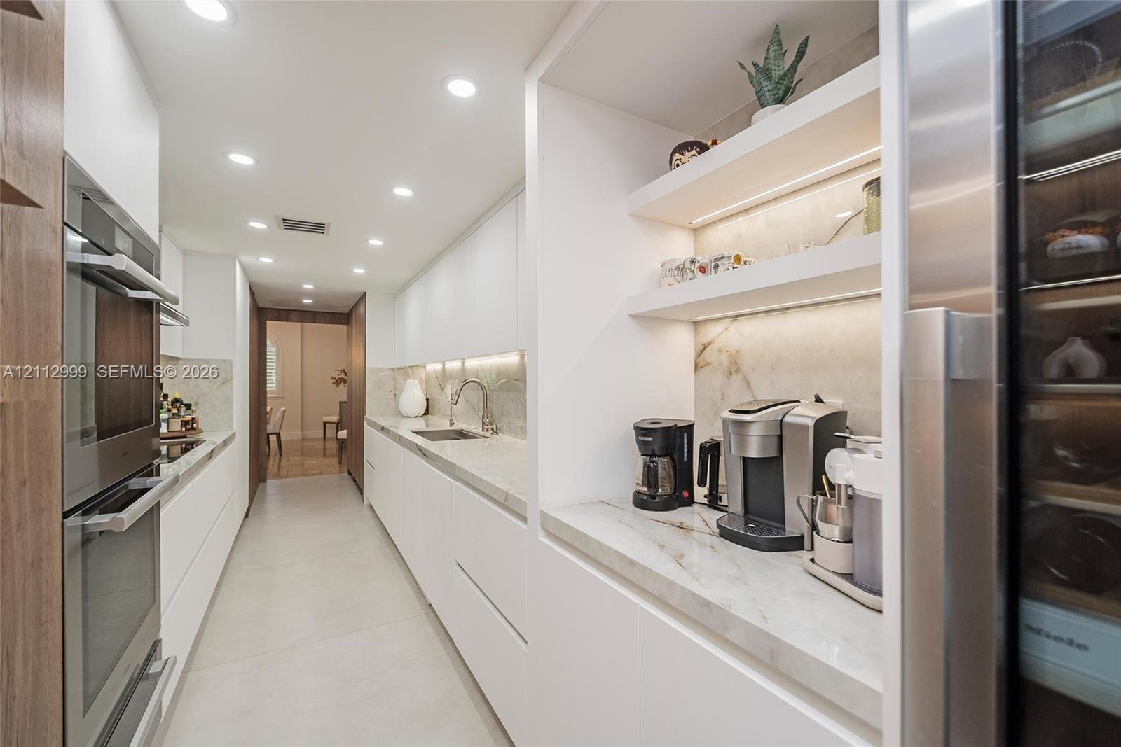 Sleek kitchen featuring flat-panel cabinetry, stone countertops, integrated stainless steel double wall ovens, built-in recessed shelving with under-c