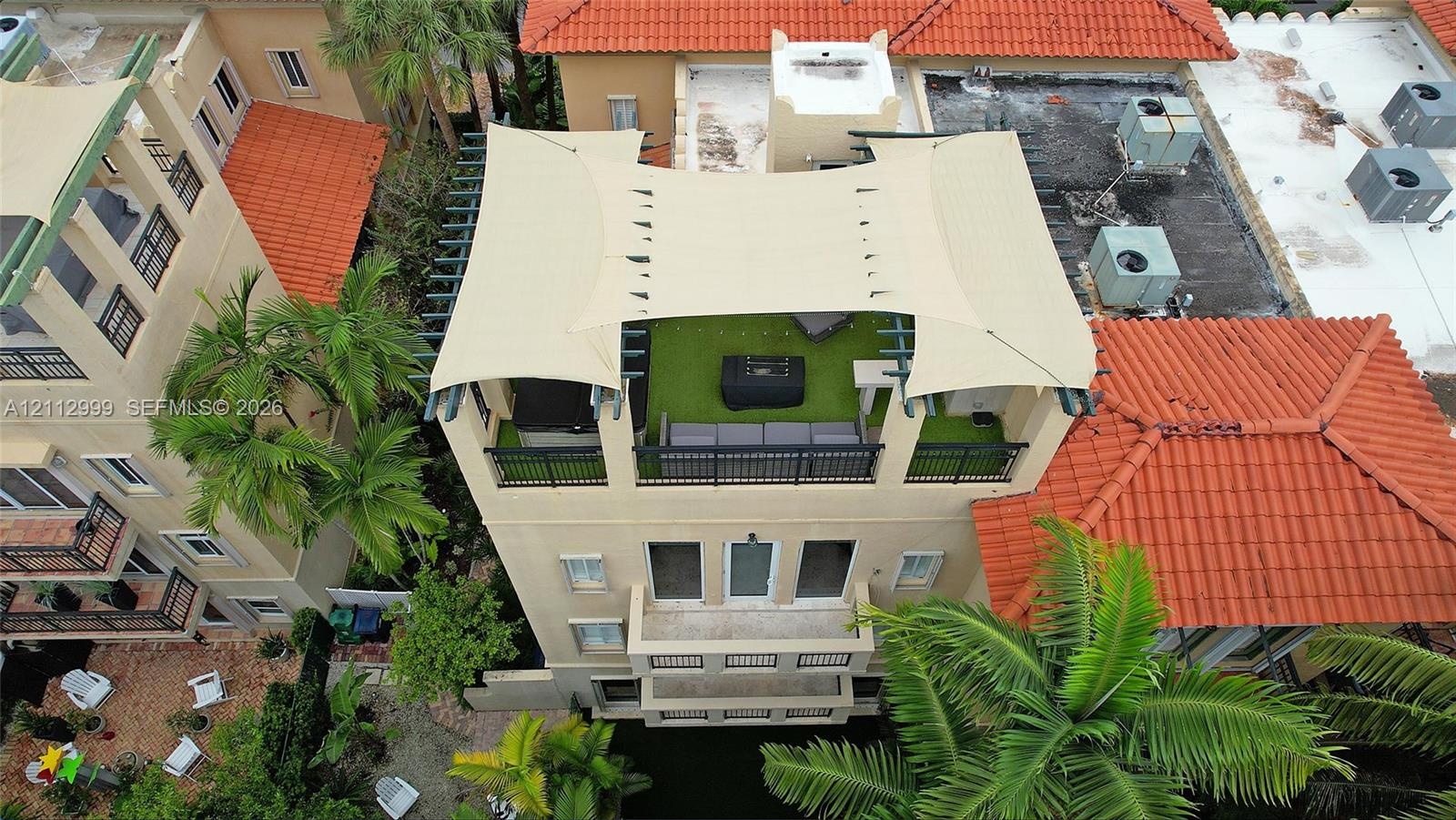 Rooftop terrace featuring synthetic turf, metal railings, and a tensile shade canopy, complemented by multiple lower-level balconies and terracotta ro