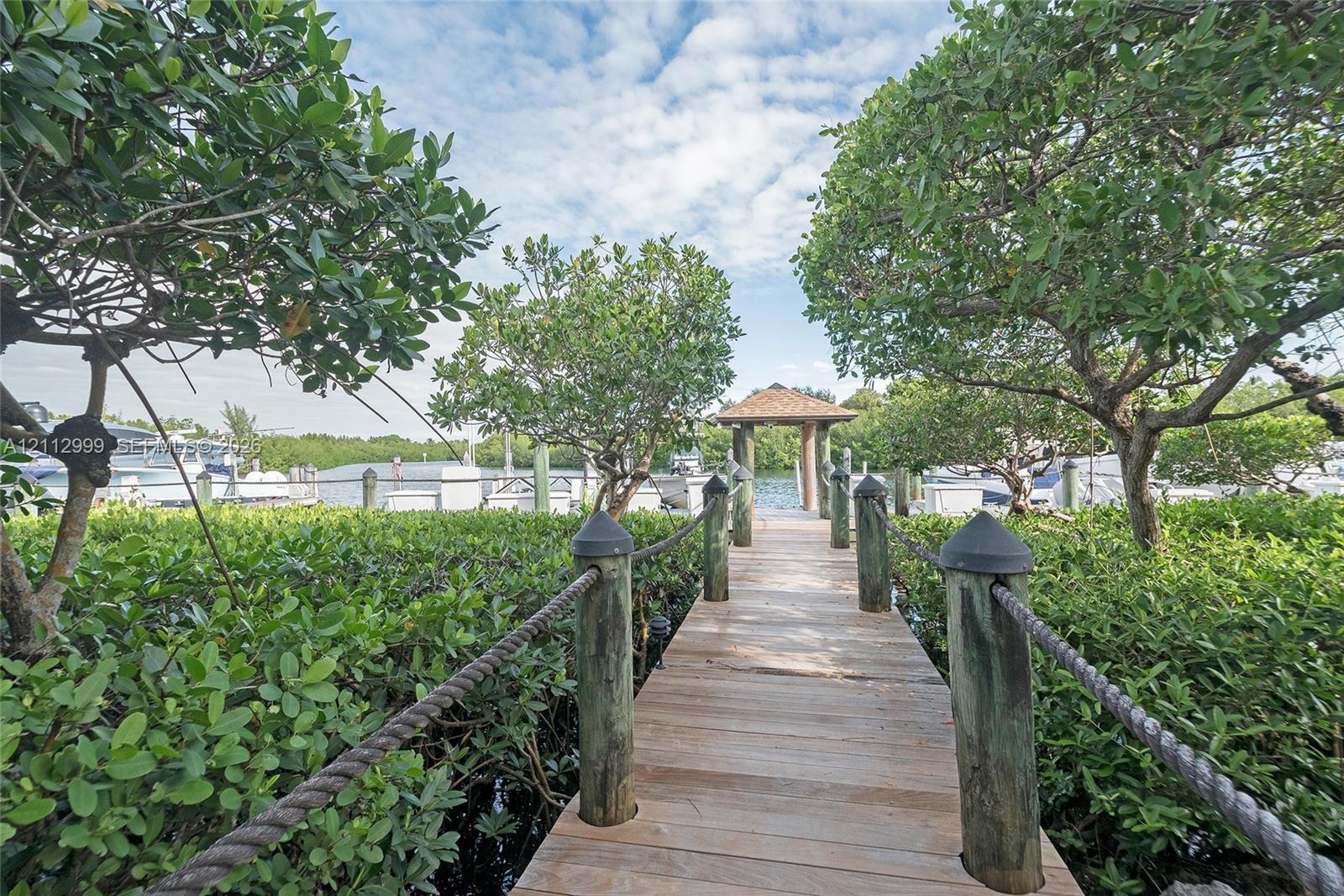 Wood-plank dock featuring post-and-rope railings, a covered gazebo terminal, and mature vegetation
