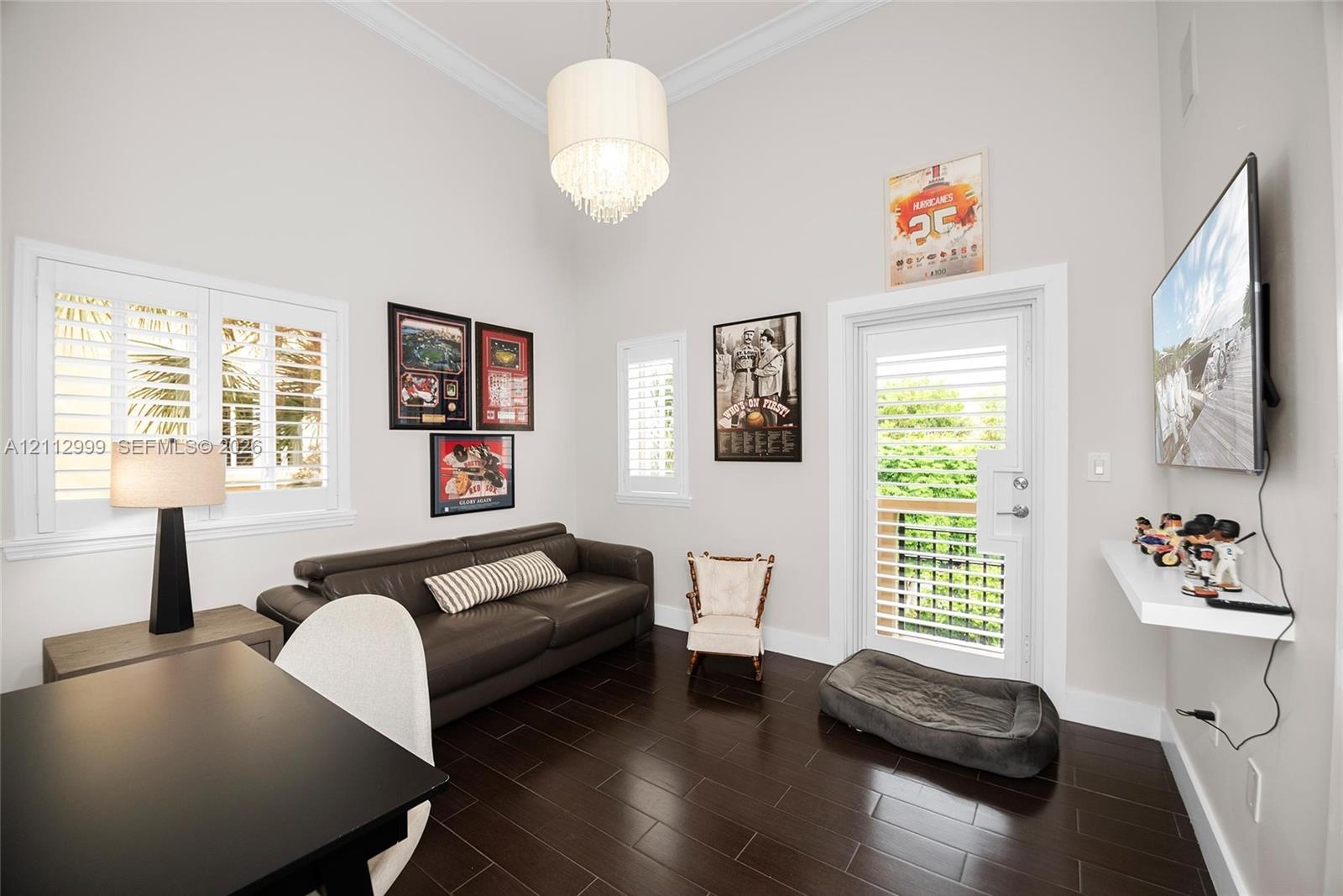 Vaulted ceilings, dark wood-finish flooring, plantation shutters, a multi-tiered crystal pendant light fixture, and a glass-paneled exterior door