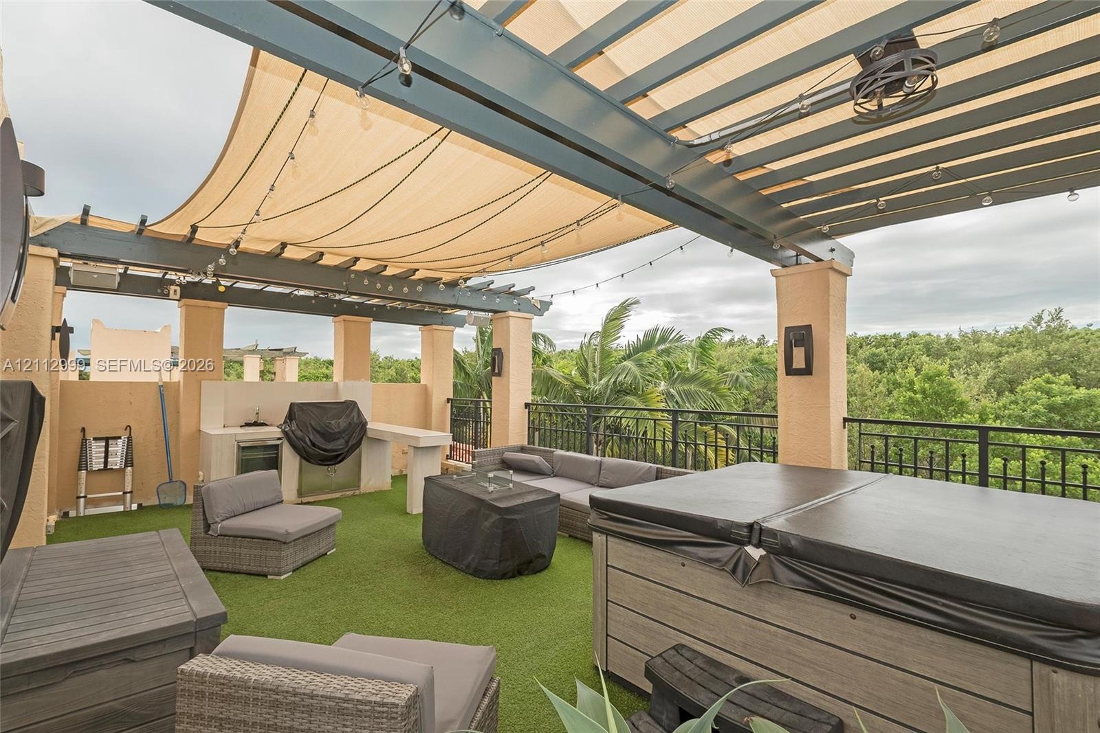Rooftop terrace featuring a covered pergola with a retractable shade canopy, built-in outdoor kitchen, integrated lighting, and a composite-finish hot