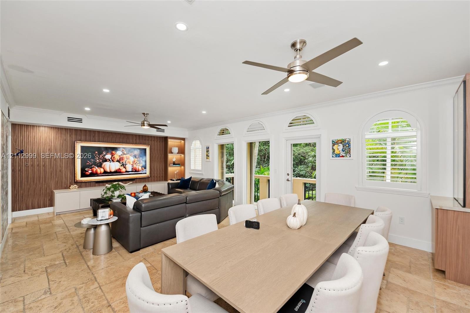 Living area featuring tile flooring, wood-finish wall paneling with integrated shelving, recessed lighting, ceiling fans, and arched windows with plan