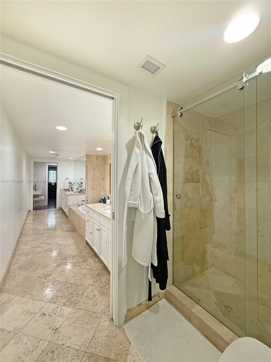 Bathroom featuring large-format tile flooring, a glass-enclosed shower with stone tile surround, and built-in cabinetry with a stone countertop