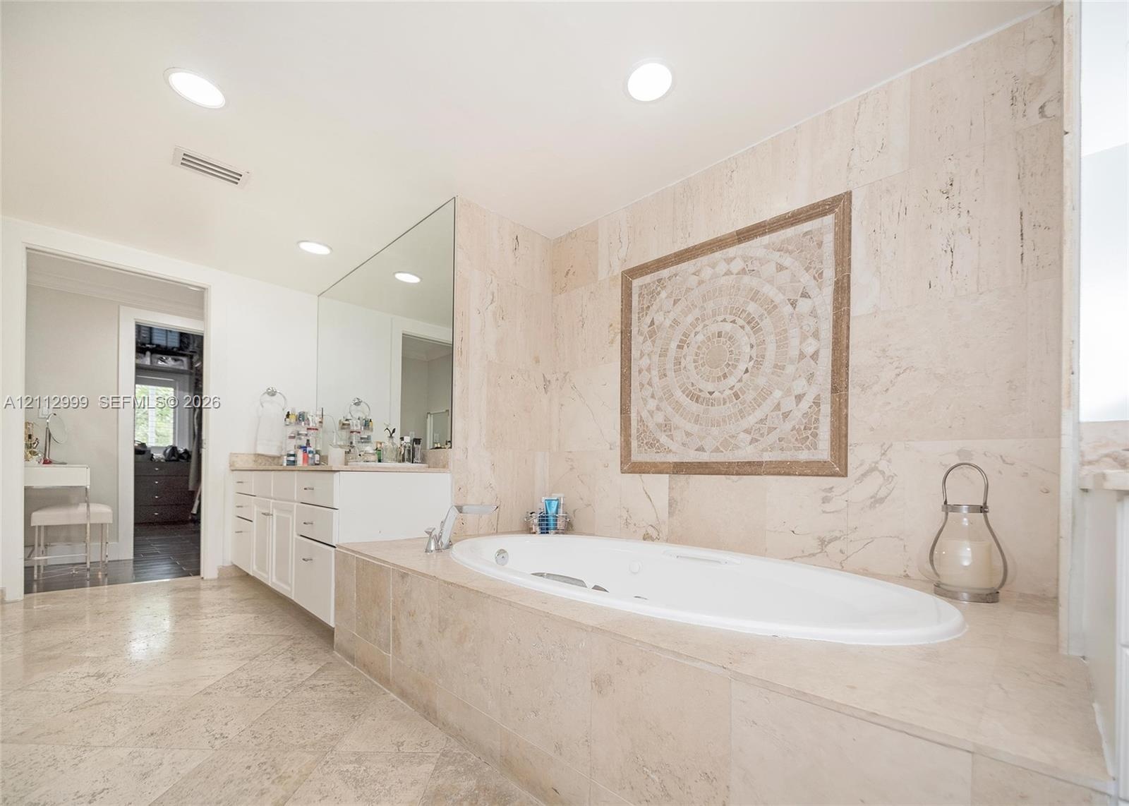 Soaking tub with a deck surround featuring stone tile cladding, wall-mounted mosaic tile inlay, recessed lighting, and stone flooring