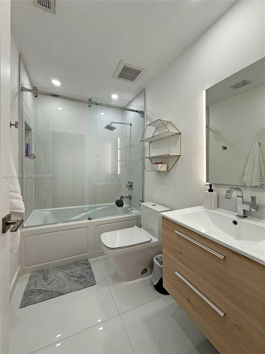 Bathroom featuring a wood-finish floating vanity with a white integrated sink, glass-enclosed shower and tub combination with a rain-style showerhead,