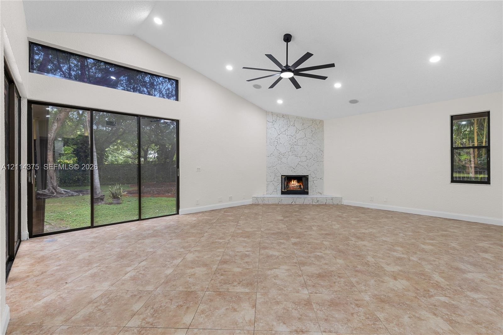 Vaulted ceilings featuring recessed lighting, expansive glass sliding doors, floor-to-ceiling stone-faced fireplace with a raised hearth, and neutral 