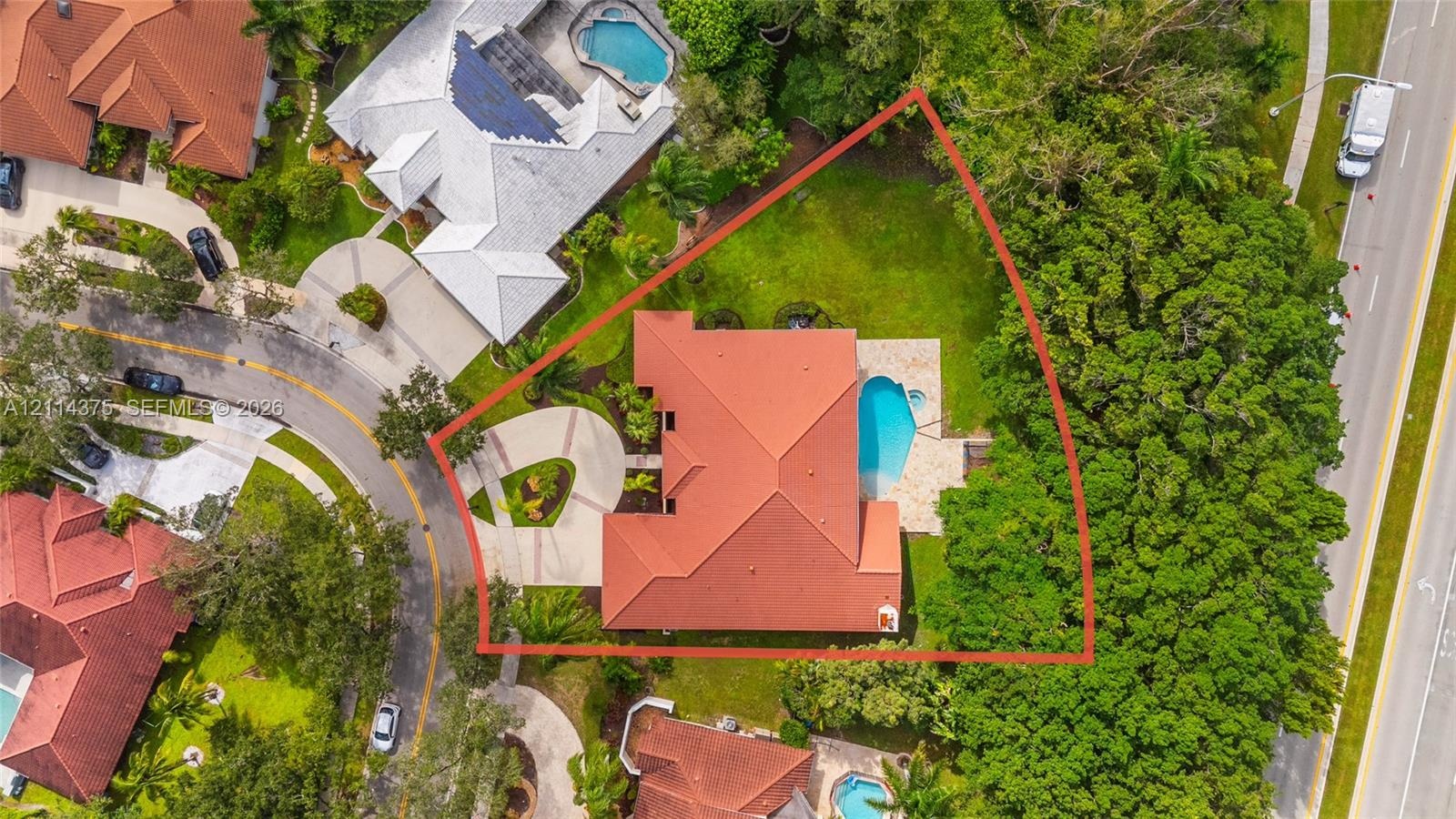 Aerial perspective of a property featuring a tile roof, a paved circular driveway, a rear swimming pool, and mature landscaping