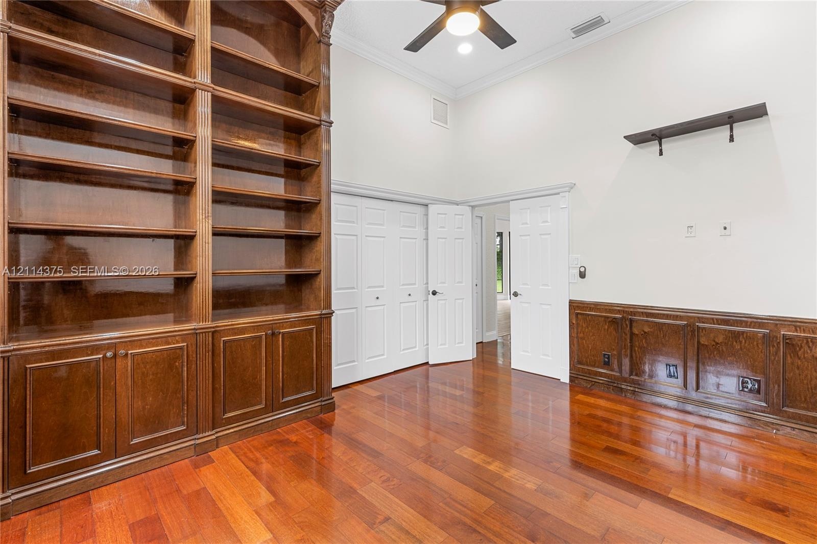 High-ceiling room featuring built-in floor-to-ceiling wood shelving, stained wood wainscoting, wood-finish flooring, and crown molding