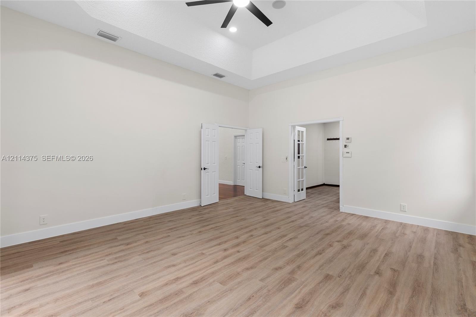Interior room featuring a high tray ceiling, wood-finish flooring, a ceiling fan with integrated lighting, French doors, and multi-panel interior door