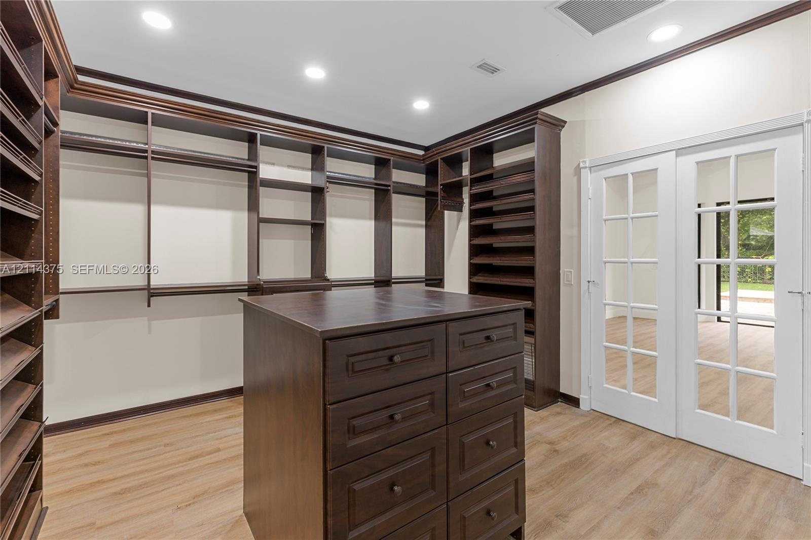 Custom storage cabinetry featuring extensive shelving, a central island with integrated drawers, wood-finish flooring, recessed lighting, and white Fr