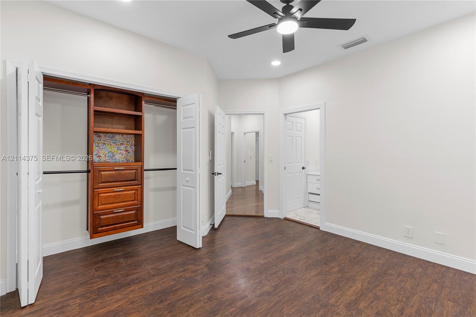 Wood-finish flooring, closet with built-in wooden cabinetry, multi-panel doors, and a ceiling fan with integrated lighting