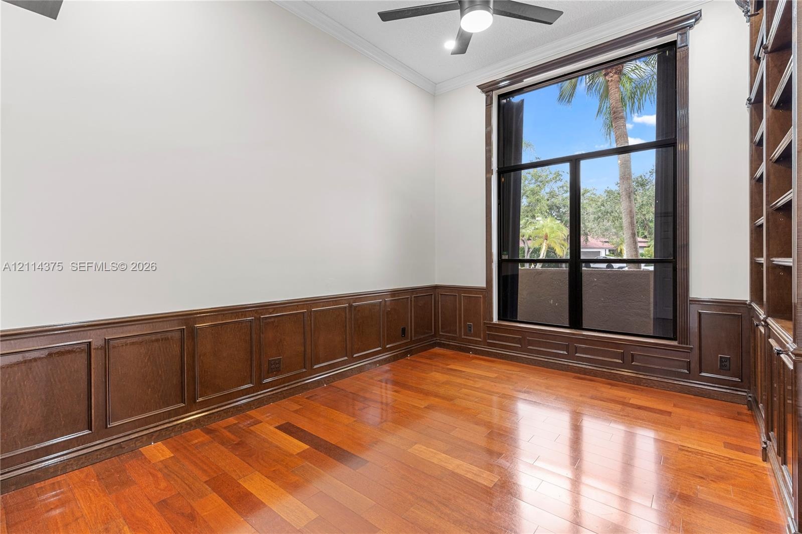 Wood-finish flooring, custom dark wood wall paneling, full-height built-in shelving, floor-to-ceiling windows, and crown molding