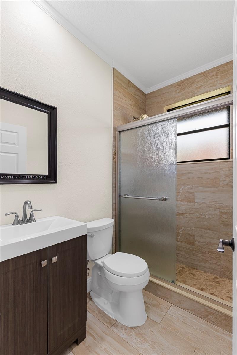 Bathroom featuring a dark wood-finish vanity, integrated rectangular sink, brushed chrome fixtures, stone-style tiled shower enclosure with sliding gl