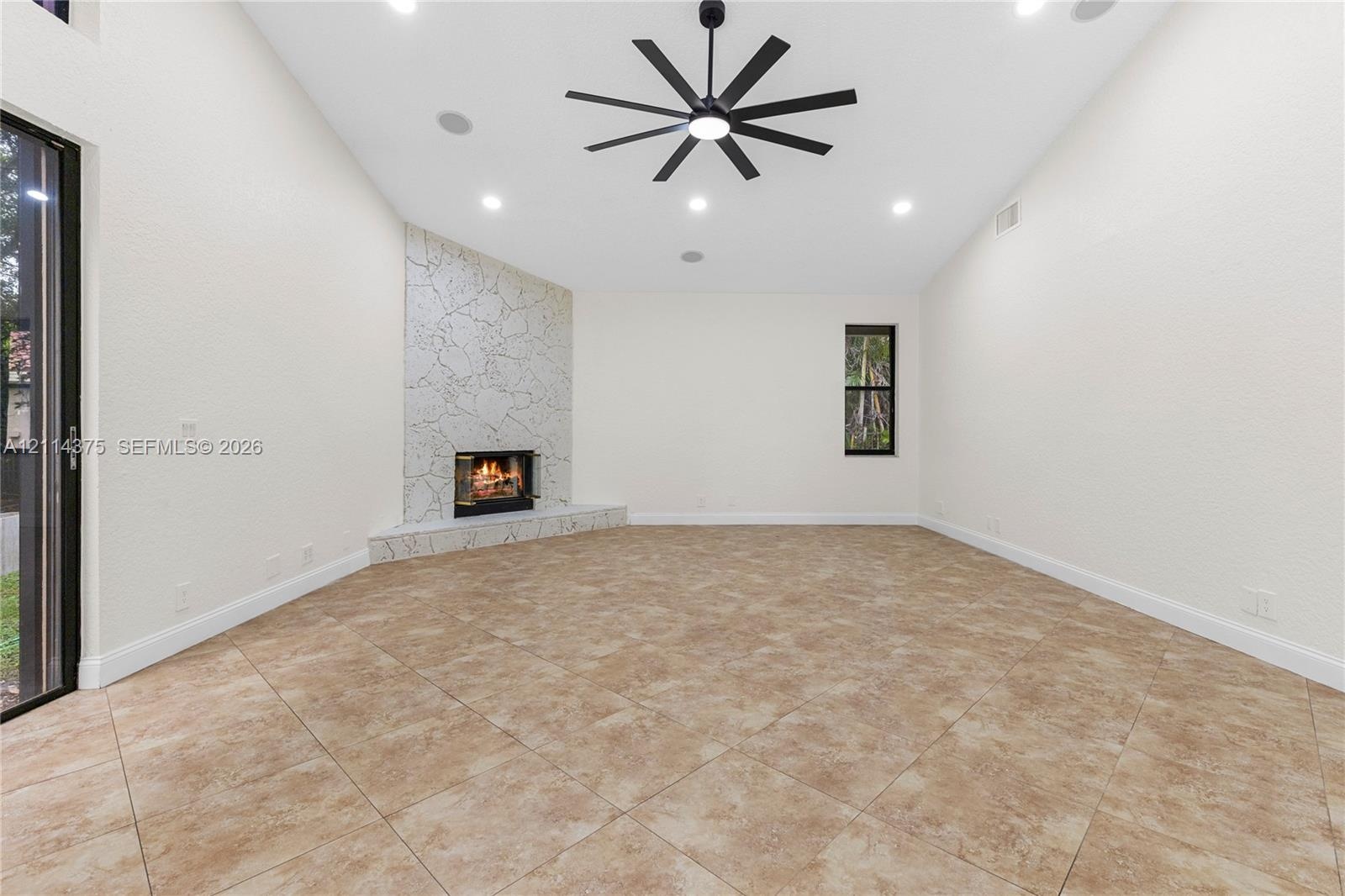High vaulted ceilings, tile flooring, stone-accented corner fireplace, multi-blade ceiling fan, and large-format sliding glass doors