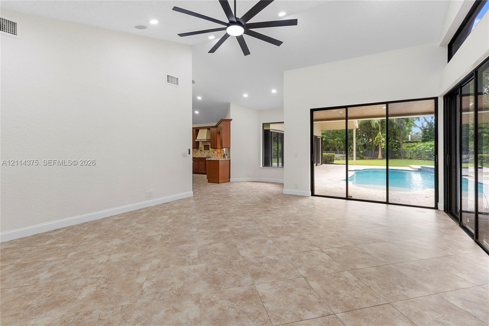 High ceilings with a multi-blade ceiling fan, large-format tile flooring, and expansive sliding glass doors opening to a private pool