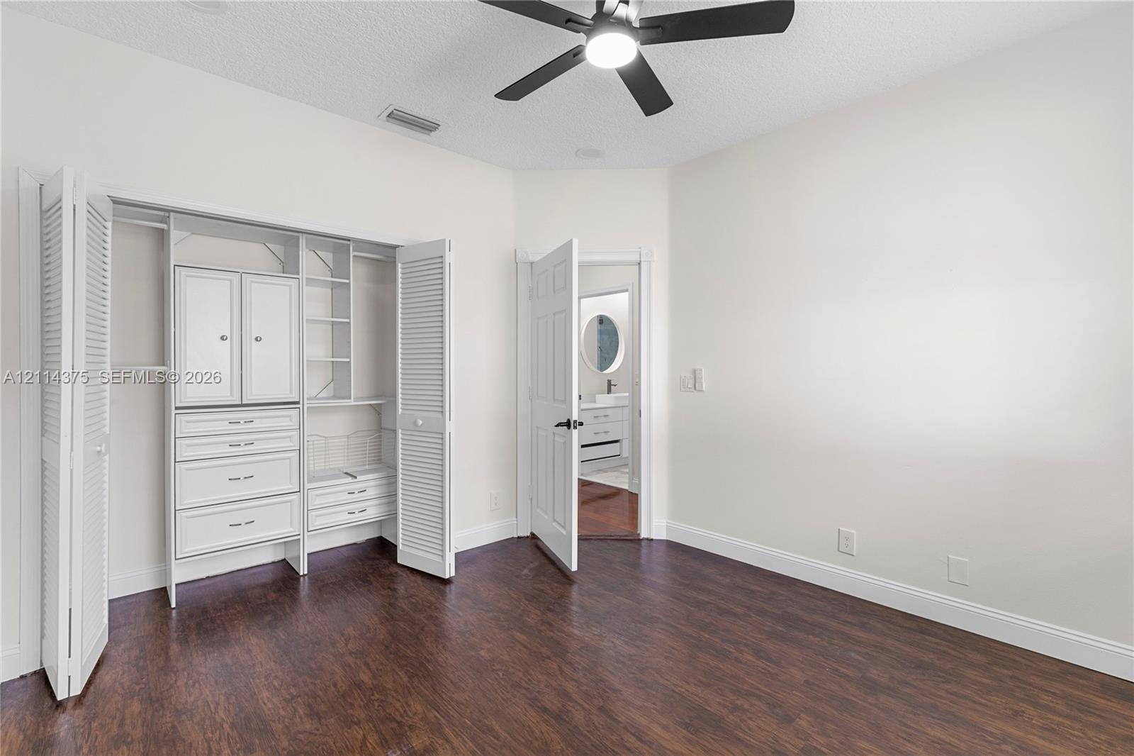 Wood-finish flooring, custom built-in closet cabinetry with drawers and shelving, and a matte black ceiling fan