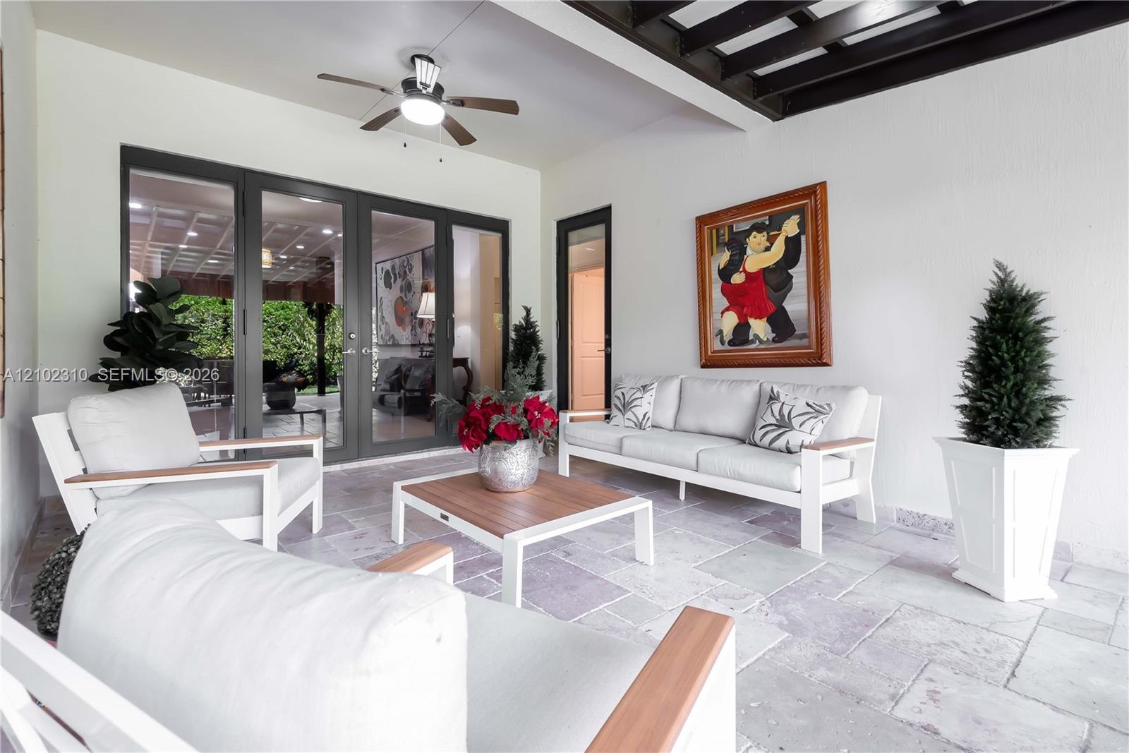 Covered patio featuring stone-tile flooring, a dark-finished wood beam ceiling, multi-panel glass door entry, and a ceiling fan