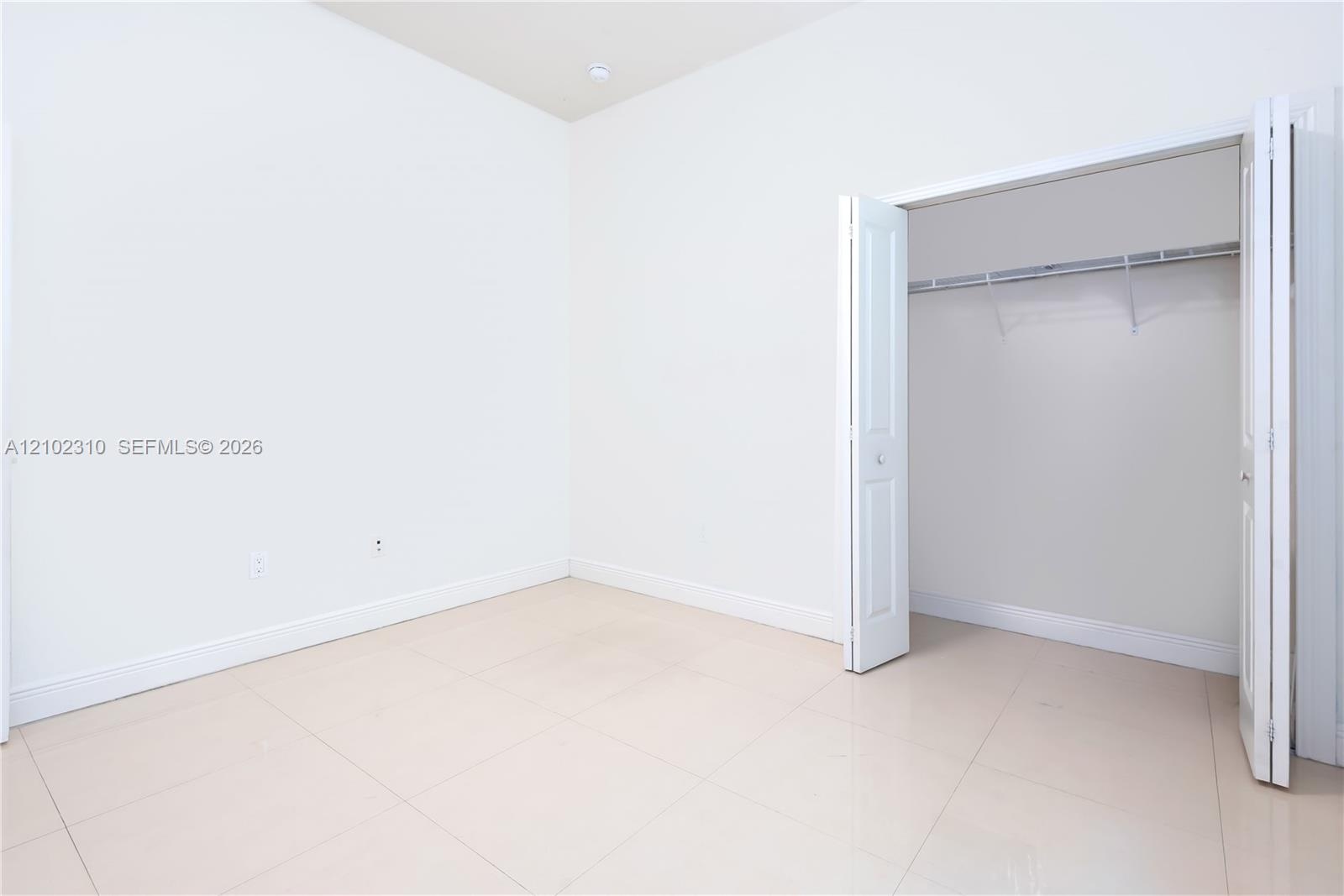 Neutral-toned large-format tile flooring, high ceilings, and closet with white paneled bi-fold doors featuring an integrated metal rod and shelf