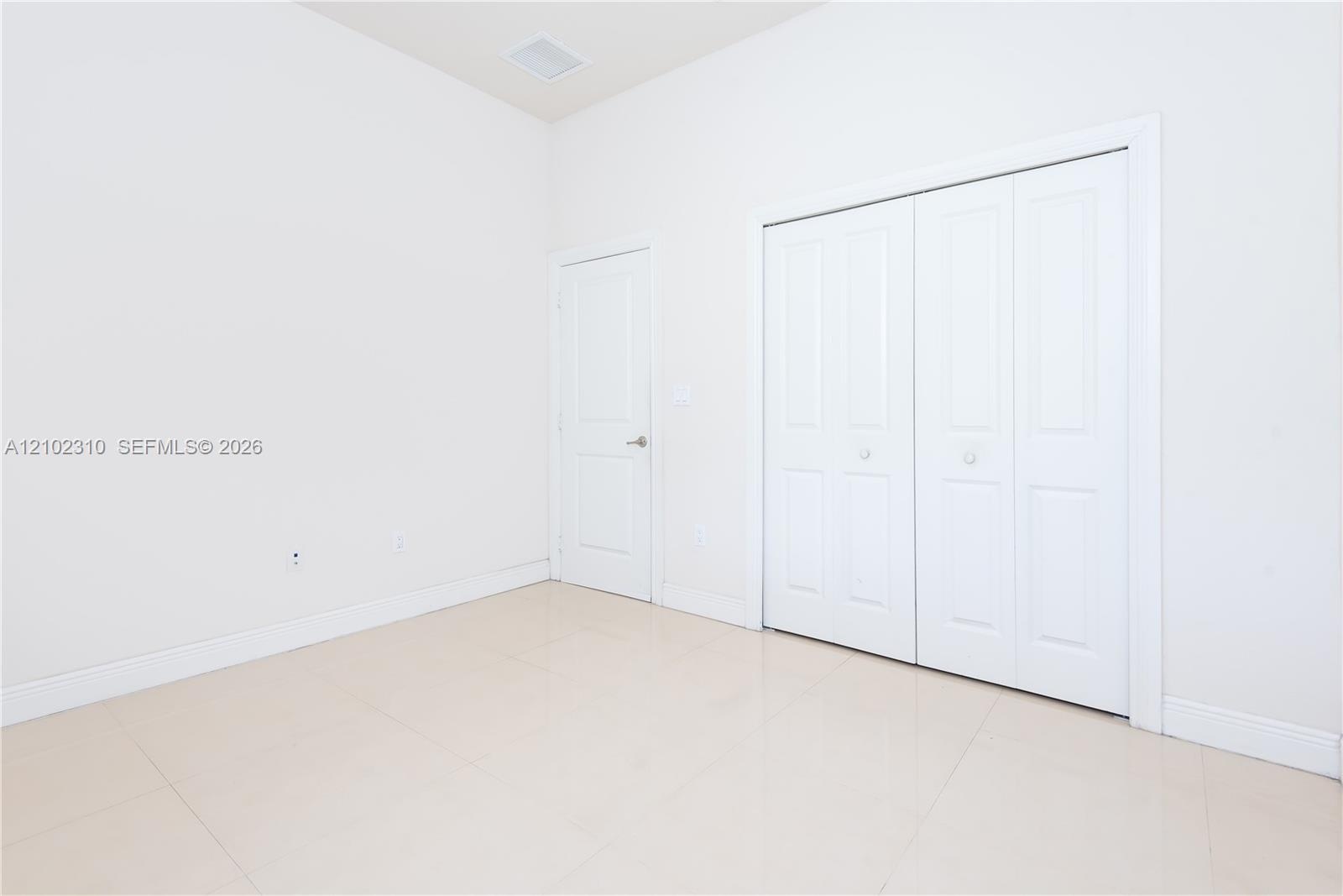 Interior space featuring neutral wall paint, polished tile flooring, a solid-panel door, and a dual-panel sliding closet