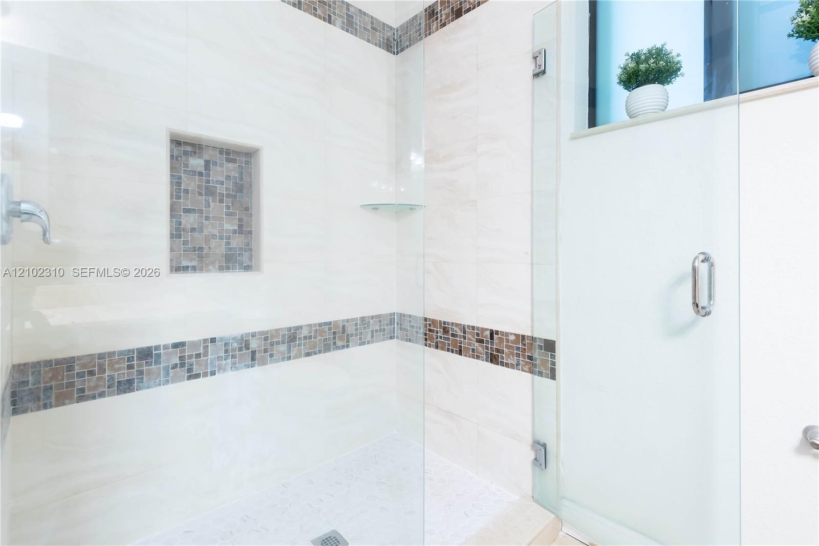 Walk-in shower featuring large-format tile walls, mosaic tile inlay, glass corner shelving, integrated wall niche, and a frameless glass door