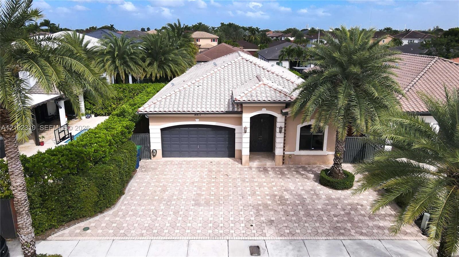 Single-story residence featuring a tile roof, paved driveway, two-car garage, and established landscaping