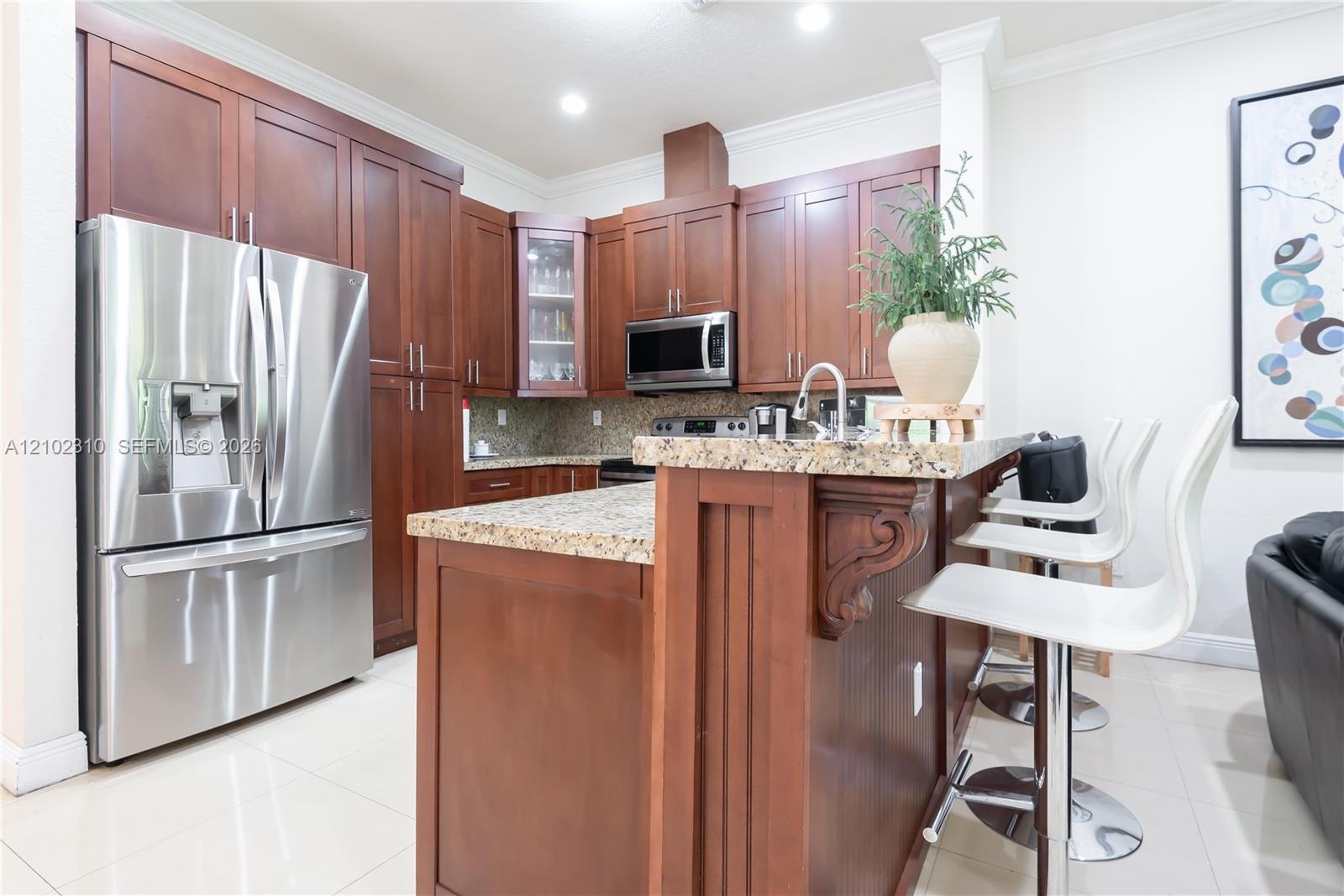 Kitchen featuring dark wood cabinetry, stone countertops, stainless steel appliances, a central island with decorative corbels, and tile flooring