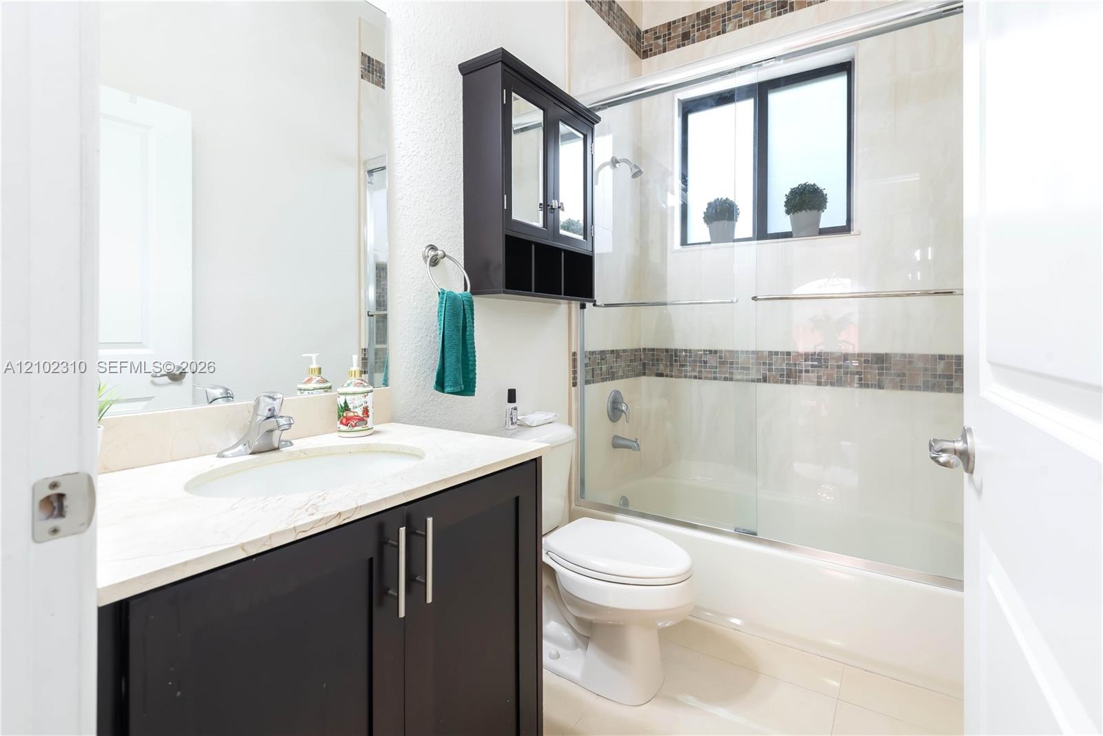 Dark-finish cabinetry vanity with stone-surfaced countertop, integrated sink, mirrored medicine cabinet, and shower-tub combination featuring tiled de