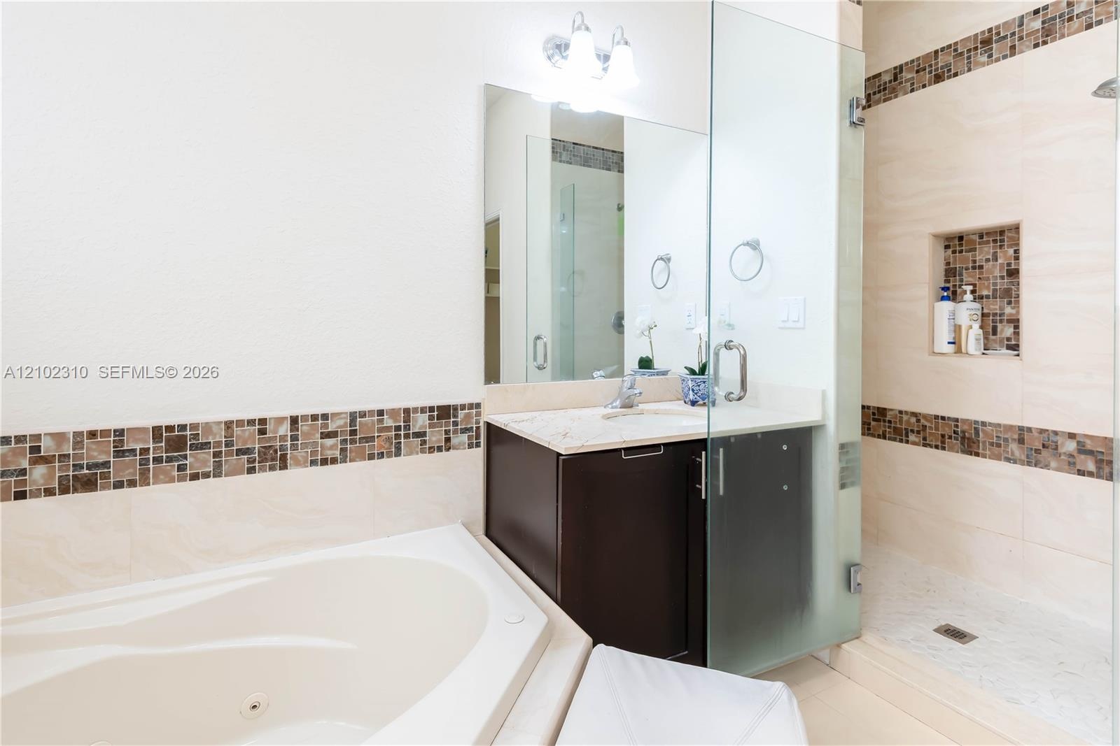 Bathroom featuring a soaking tub, glass-enclosed shower with a tiled recessed niche, vanity with a stone countertop, and decorative mosaic tile accent