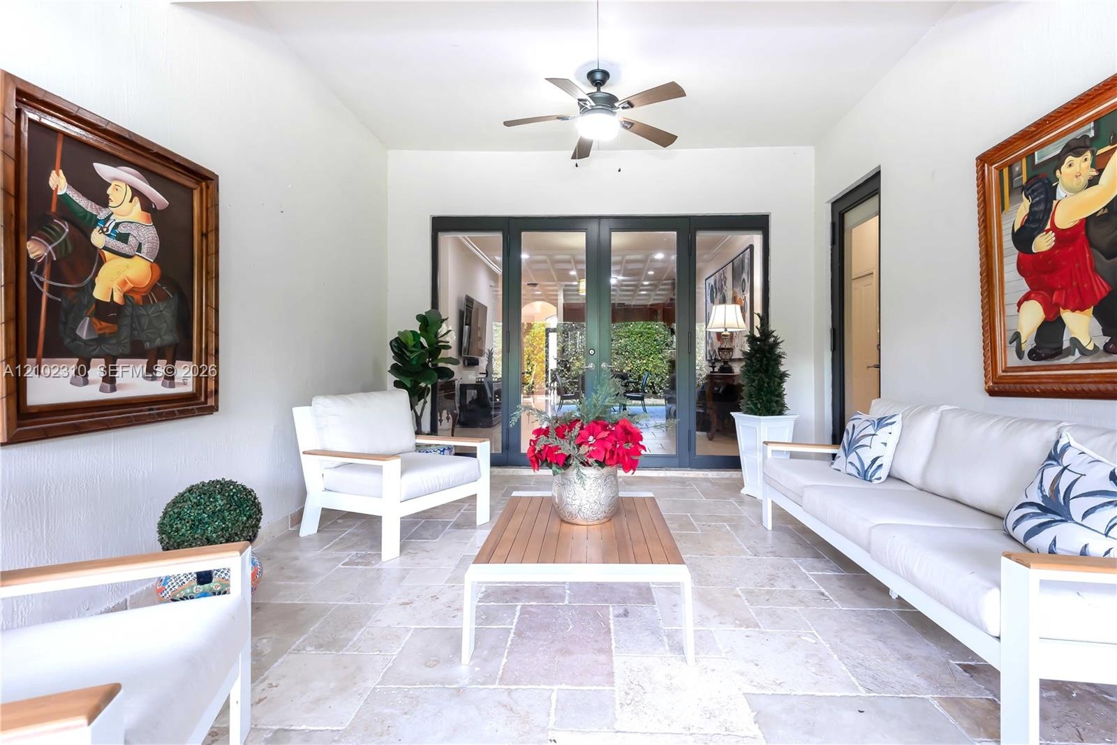 Covered patio featuring stone-tile flooring, a central ceiling fan with integrated lighting, and multi-panel glass-paned French doors