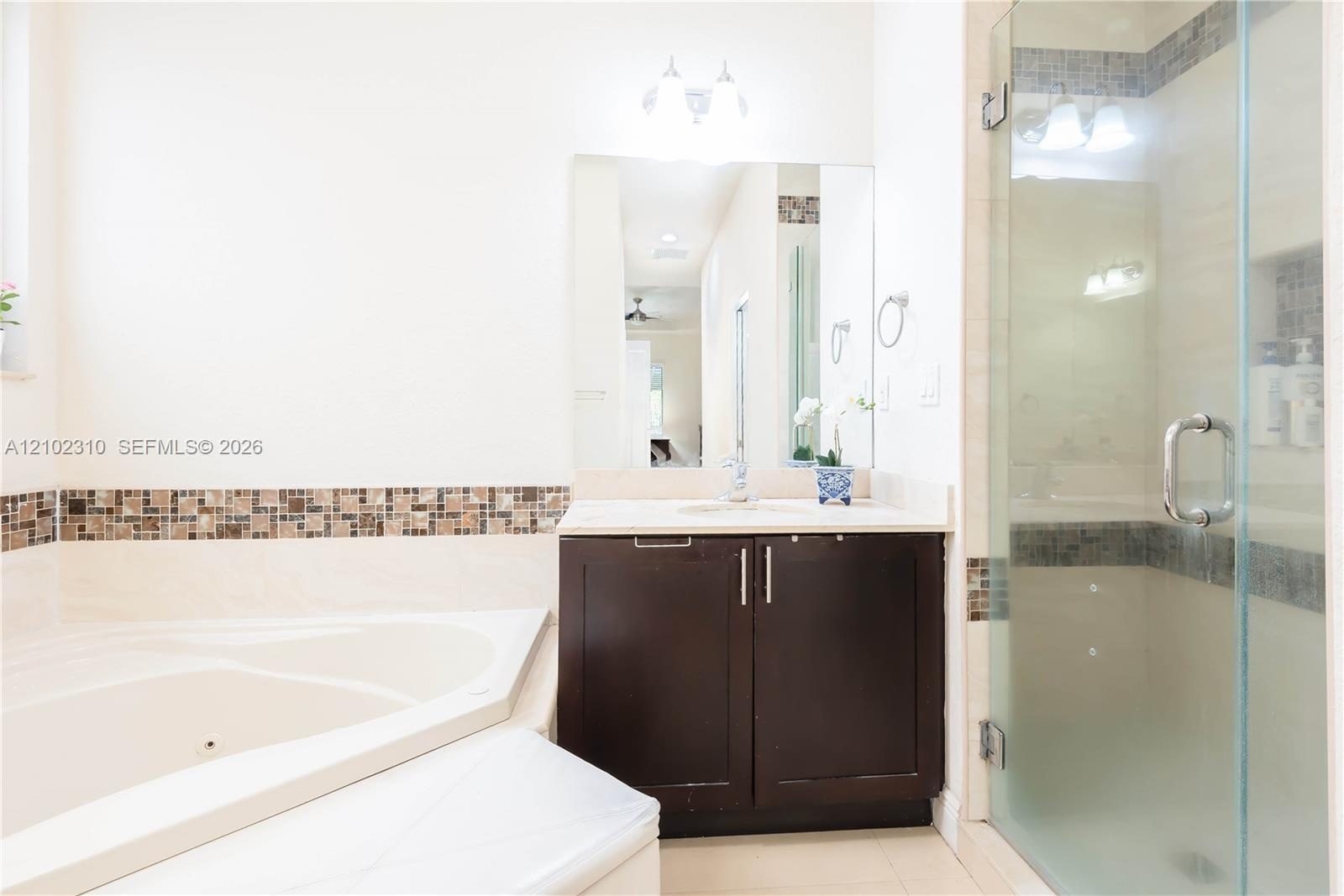 Bathroom featuring a jetted corner soaking tub, dark-finish cabinetry with a solid surface countertop, an integrated sink, and a glass-enclosed shower