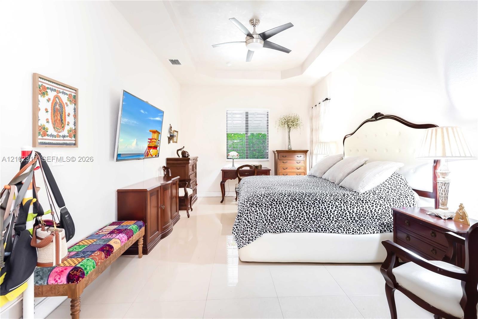 Room featuring high tray ceilings, large-format tile flooring, and a ceiling fan with integrated lighting
