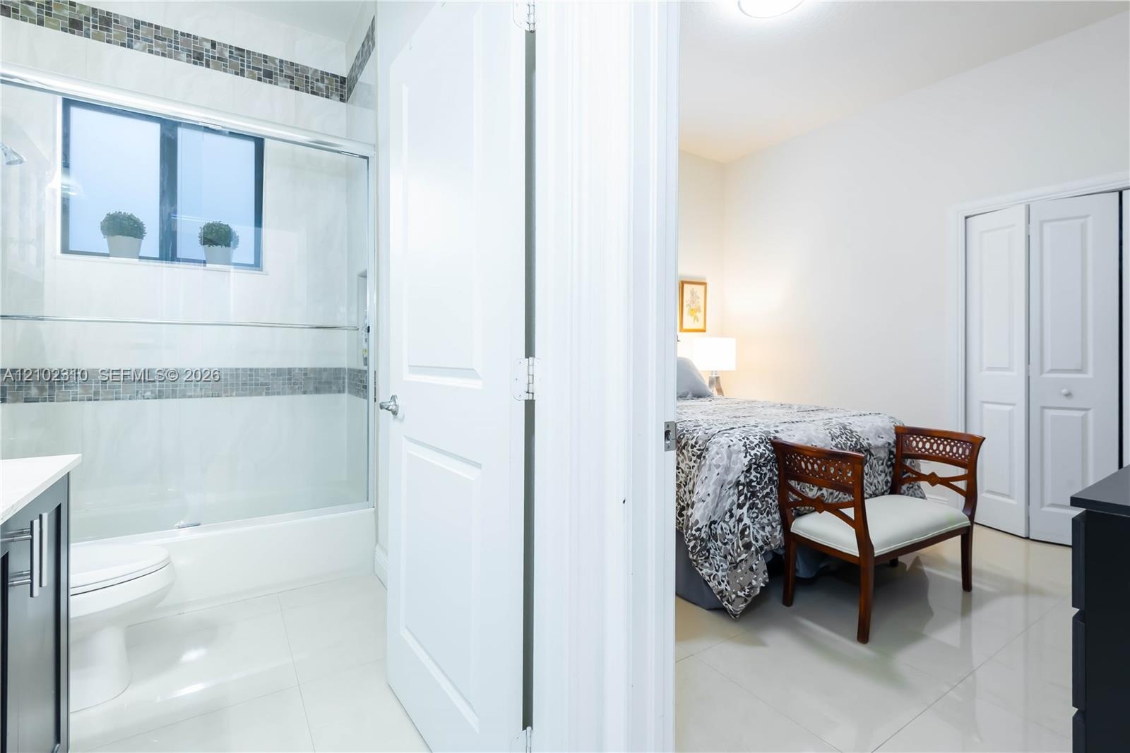 Bathroom featuring a glass-enclosed shower with decorative mosaic tile inlay, large-format tile flooring, and a white vanity