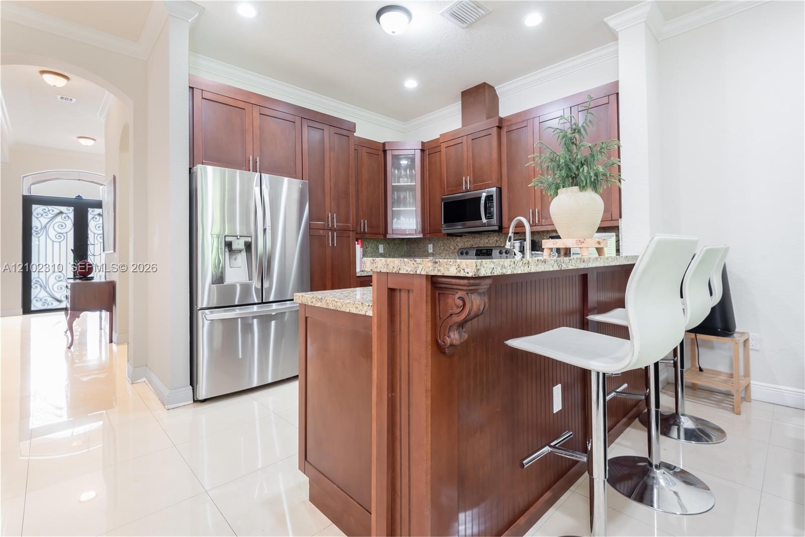 Kitchen featuring wood cabinetry, stone countertops, stainless steel appliances, a raised bar, and tile flooring