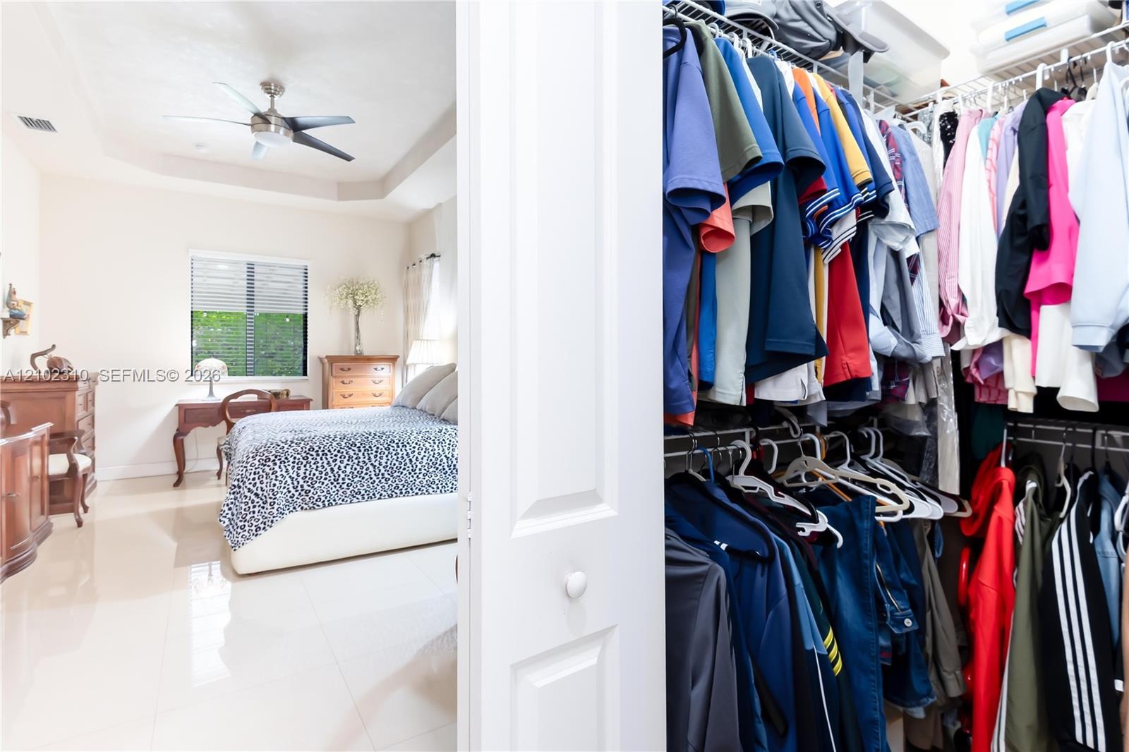 Walk-in closet featuring tiered wire shelving and a multi-room perspective including polished tile flooring, a tray ceiling, and a ceiling fan
