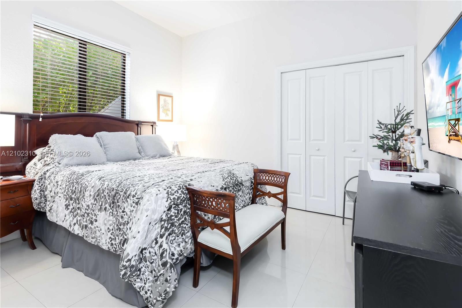 Bedroom featuring large-format tile flooring, multi-panel window with horizontal blinds, and bi-fold closet doors