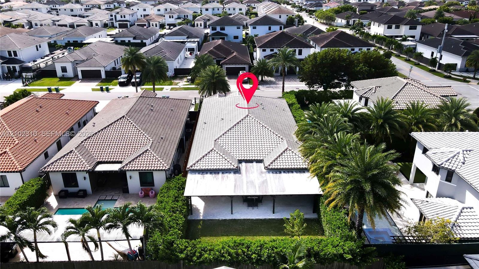 Aerial perspective of a residence featuring a tiled roof, a rear covered patio, and a landscaped backyard with mature palm trees