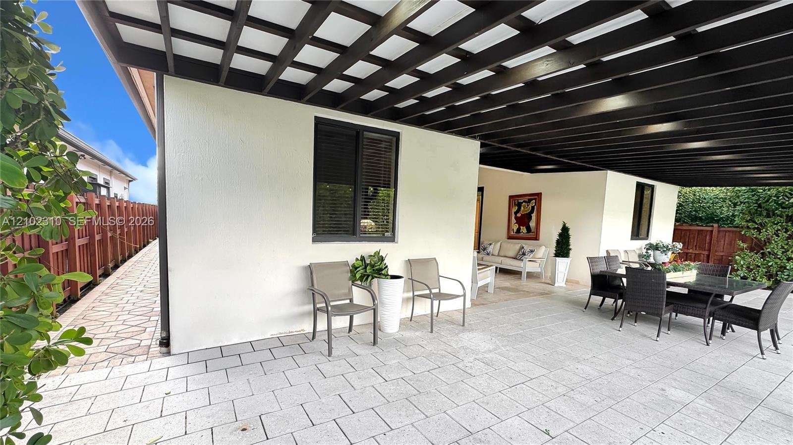 Covered patio featuring a large black pergola, light-toned stone paver flooring, stucco exterior walls, and dark-framed windows
